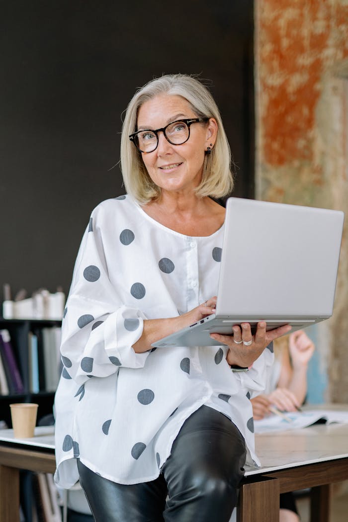 Senior woman with glasses holding a laptop, symbolizing experience and confidence in a business setting.